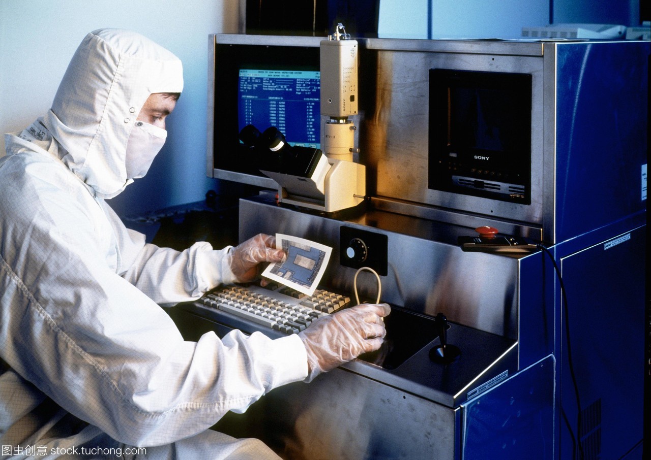 模型發(fā)布。硅晶片檢查。一名技術人員拿著一張硅片的部分照片,同時對其微電路進行檢查。他坐在顯微鏡下觀察晶圓的放大。這是一個&ldquo;干凈的房間&rdquo;,技術人員穿著一套身衣,兜帽和面罩。在所有過程涉及人工微電路的制作和測試技術人員穿防護服和手套空氣潔凈室的過濾。即使是最小的塵埃微粒也可能破壞其中的一個微電路。